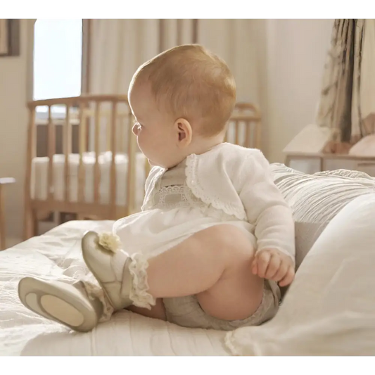 Bambino seduto su letto con cardigan cerimonia bambino bianco Mayoral in ambiente luminoso e accogliente