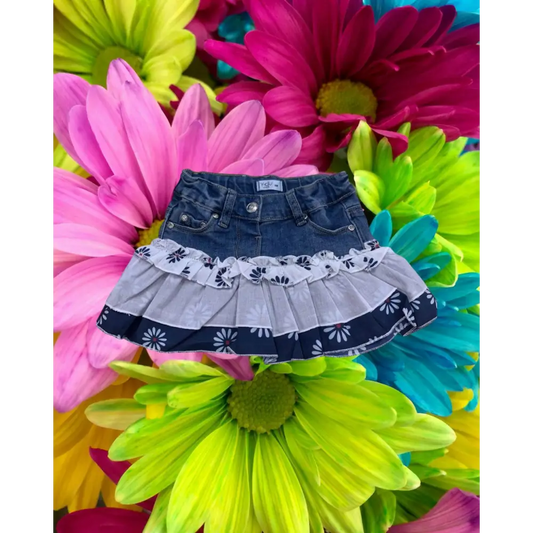 Gonna denim bimba 6 mesi Y-Clù con balze e dettagli floreali su sfondo di fiori colorati