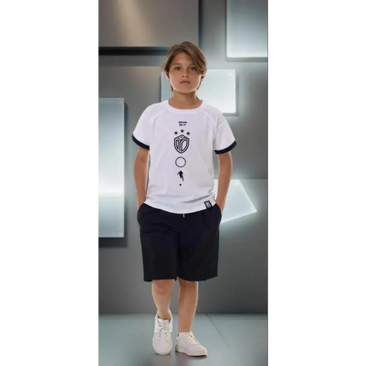 Maglietta Bikkembergs bambino bianca con stampa nera indossata da bambino in piedi con pantaloncini neri