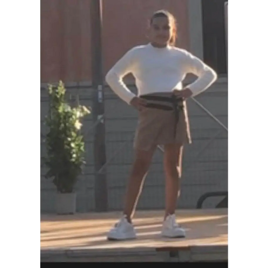 Modella Y Clu con gonna marrone corto a portafoglio maglione bianco e sneakers su palco gonna ragazza 8 16 anni