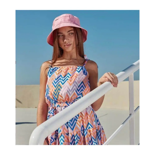 Ragazza con abito fantasia bambina Paris Hilton multicolore a zigzag e cappello rosa appoggiata al corrimano bianco