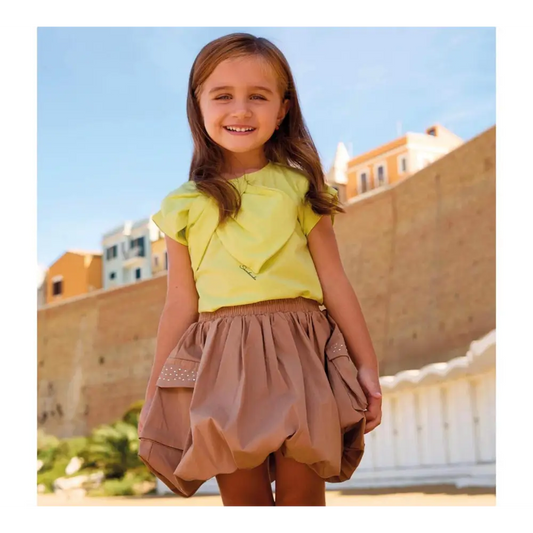 Bambina sorridente che indossa una gonna a palloncino per bambina sarabanda color beige all'aperto