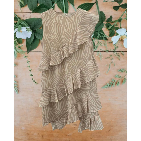 abito bambina stampa zebrata in chiffon beige con balze a volant asimmetrico su sfondo legno e foglie