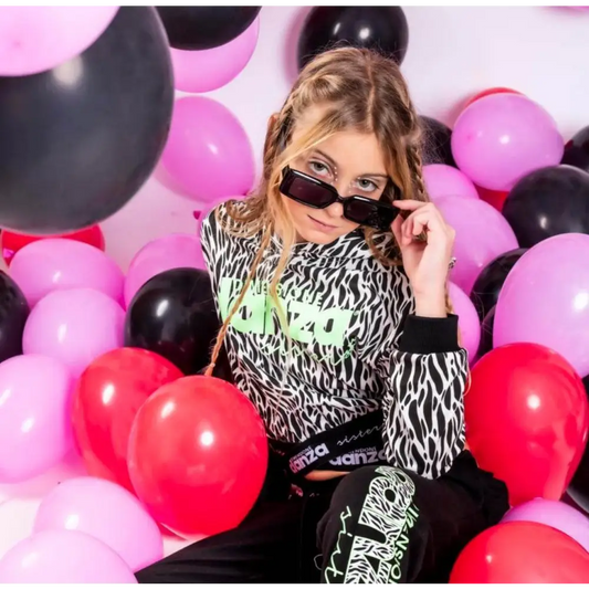 Ragazza con occhiali indossa felpa corta ragazza Dimensione Danza stampa zebra in festa tra palloncini rosa e neri