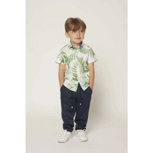 Bambino con camicia bambino fantasia foglie verde Y Clu a maniche corte abbinata a pantaloni blu e sneakers bianche