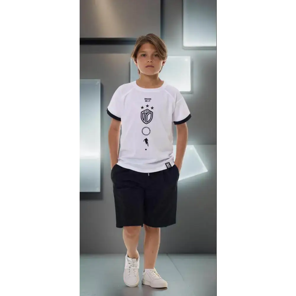 Maglietta Bikkembergs bambino bianca con stampa nera indossata da bambino in piedi con pantaloncini neri