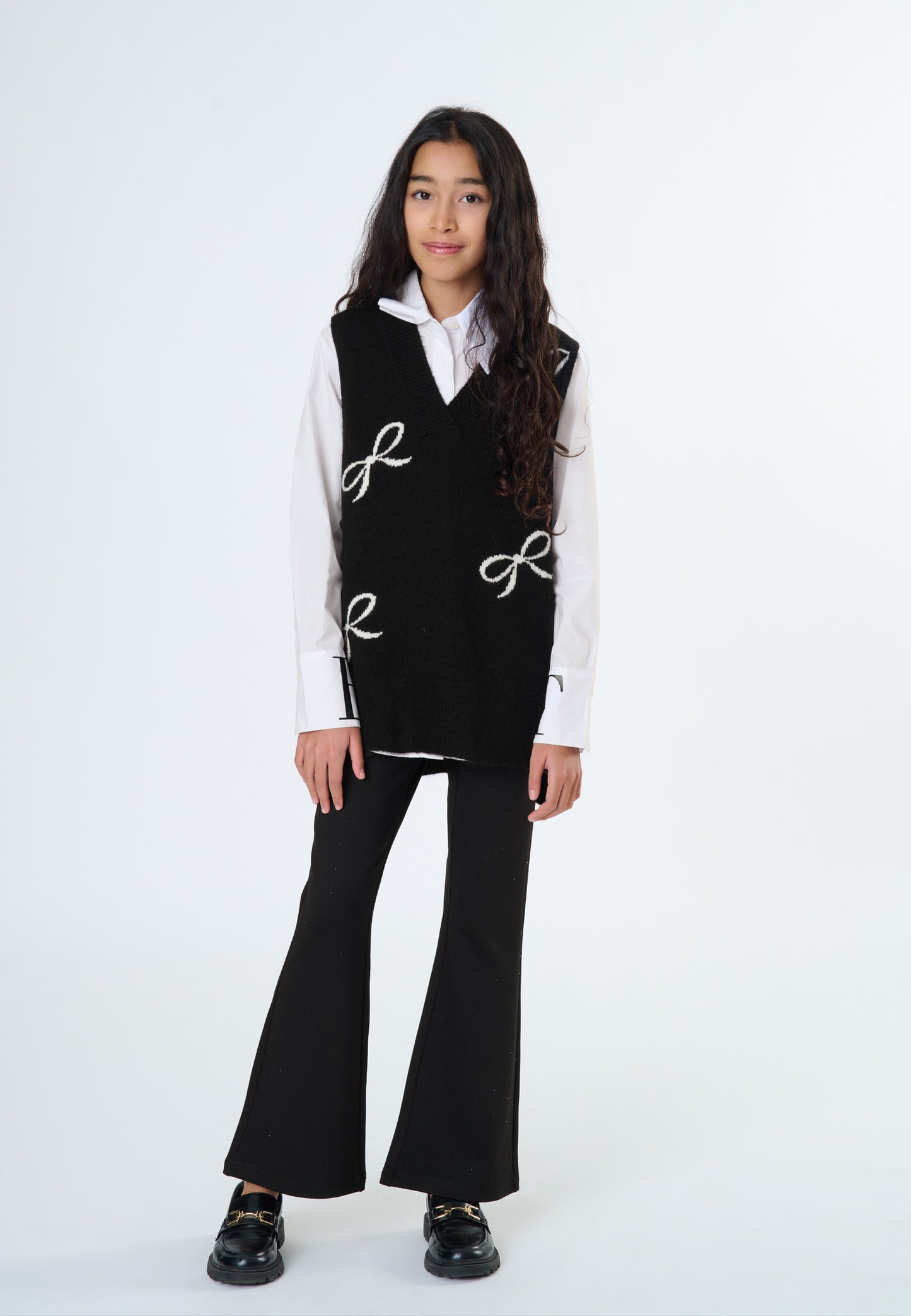 Ragazza che indossa pantaloni neri a zampa con top nero e camicia bianca, look elegante e alla moda