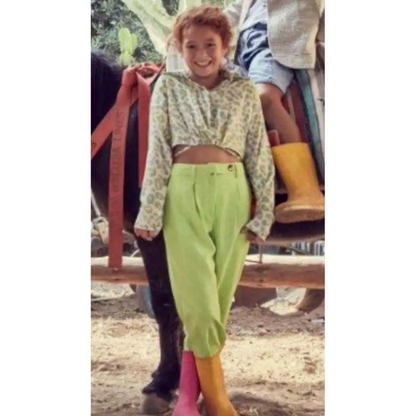 Bambina sorridente con camicia corta maculata bambina Y Clu abbinata a pantaloni verdi vita alta e stivali colorati